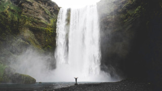 A huge waterfall in the background and a small figure standing at the bottom, raising their arms.